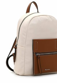 Petit sac à dos avec corps en tissu beige, poche avant marron avec fermeture éclair, coutures blanches, poignée visible et deux bretelles réglables.