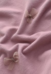 Rosa Stoff mit einer sanften Textur, der zwei kleine, hellfarbene Tüllschleifen zeigt. Das Material ist glatt und leicht dehnbar, wodurch sanfte Falten entstehen.