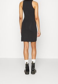 Svart ärmlös klänning med en åtsittande design, matchad med svarta ankelstövlar och vita strumpor. Slät tyg med en enkel, odekorerad stil.