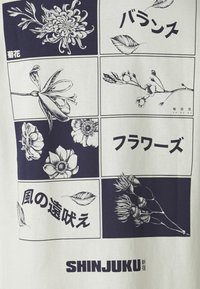 White fabric T-shirt featuring dark floral illustrations and Japanese text. Graphics include various flowers in a grid layout. Text reads "SHINJUKU."