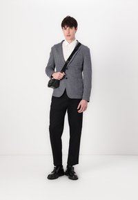 Γκρίζα υφασμάτινη σακάκι πάνω από ένα λευκό πουκάμισο, μαύρο παντελόνι και μαύρα παπούτσια. Το μοντέλο κρατά μια μικρή μαύρη τσάντα χιαστί. Μινιμαλιστικός σχεδιασμός.