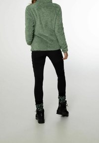 Zielony polar z wysokim kołnierzem w połączeniu z czarnymi legginsami. Stylizacja zawiera wzorzyste zielone skarpetki i czarne, masywne botki.