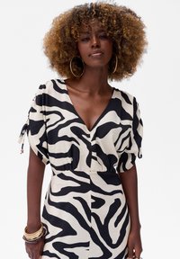 Zwart en crèmekleurig zebra print jurk met een diepe V-hals, korte pofmouwen en strikken verfraaid met kralen. Glad, lichtgewicht materiaal.