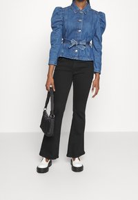 Džínová bunda s nafouknutými rukávy, předními knoflíky a páskem v pase. Nosit s černými zvonovými kalhotami, bílými platformovými botami a malou černou taškou.