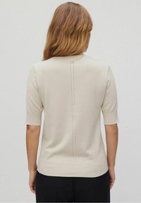 Top de punto de manga corta en color beige, con escote redondeado, una costura central en la parte posterior y detalles acanalados en el dobladillo y las mangas.
