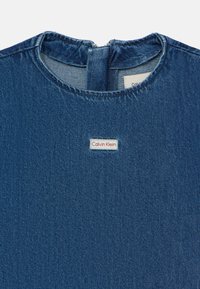 Denim top in dark blue with a round neckline, featuring a back zipper and a Calvin Klein label in red and white on the front.