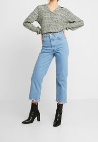 Grön mönstrad blus med lång ärm, ljusblå jeans med hög midja och svarta klackstövlar med dragkedja. Klassisk passform och avslappnad stil.