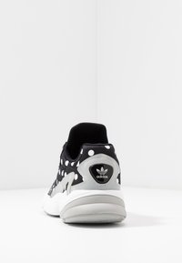 Svart och vit prickig sneaker med vadderad krage, texturerad ovandel, kraftig sula och logotypdetalj på hälen.