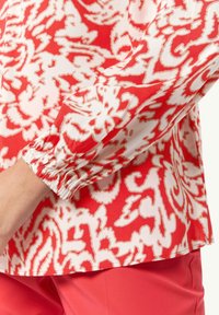 Blusa a strisce rosse e bianche con maniche arricciate e vestibilità rilassata. Il tessuto è leggero con una consistenza liscia, caratterizzato da motivi floreali.