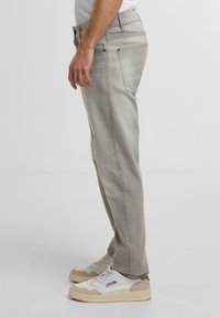 Jeans grigio chiaro a gamba dritta con una texture liscia, cinque tasche e cuciture discrete. Abbinati a sneaker beige con accenti chiari.