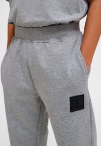 Grijze joggingbroek gemaakt van een katoenmengsel, voorzien van een elastische tailleband en een zwart vierkant logo met reliëf op de linkerzijzak.