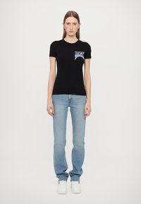 T-shirt nera a maniche corte con un design grafico blu sul petto, abbinata a jeans blu chiaro e sneaker bianche.