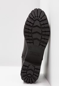 Semelle de chaussure en caoutchouc noir avec un motif de bande de roulement profond indiquant la taille 37 et la marque Tamaris.
