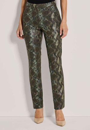 Slim-fit broek met een donkergroene en bruine slangenprint, gedragen met huidkleurige puntige hakken, getoond van taille tot voeten.