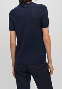 Marinblå stickad kortärmad topp med rund halsringning och en liten logotypdetalj på baksidan; har en texturerad yta och ribbad fåll.