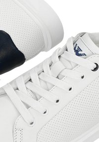 Weiße Ledersneaker mit perforierten Seitenpaneelen, weißen Schnürsenkeln und einem schwarzen Emblem auf der Zunge in der Nähe des Knöchelkragens.