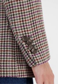 Ullblazer med houndstooth-mönster i beige, brunt och lila; har fyra mörka knappar vid ärmen och strukturtextil.