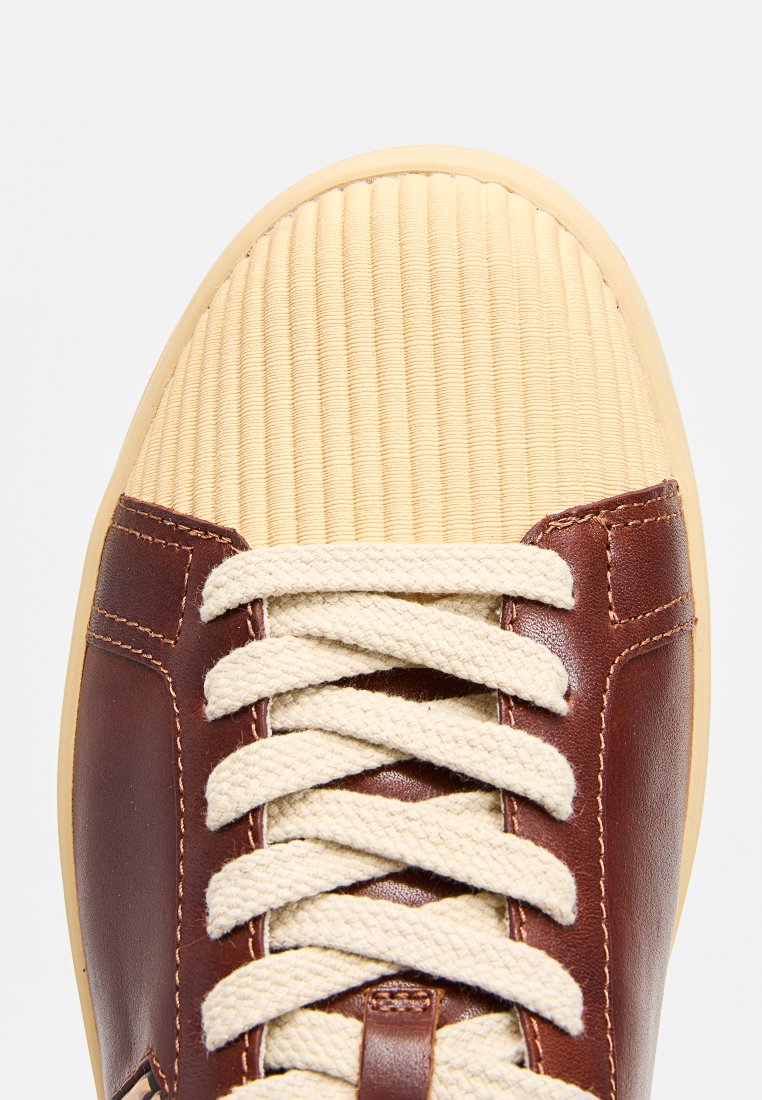 Brązowy skórzany but z beżowym prążkowanym noskiem, kremowymi sznurówkami i gładką powierzchnią. Subtelne przeszycia po bokach.