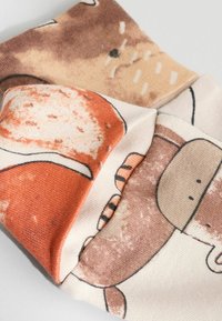 Textil mit einem orange- und braunfarbenen Tiermuster auf einem cremfarbenen Hintergrund. Der Stoff ist weich mit einer leichten Textur, gefaltet mit sichtbaren Nähten.