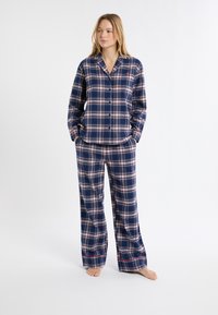 Komplet piżamy w kratkę w kolorze granatowym, z wzorami w kolorze niebieskim, białym i czerwonym. Koszula na guziki z kołnierzykiem, długie rękawy i spodnie o szerokich nogawkach. Miękki materiał.