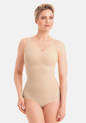 Woman with short blonde hair wearing a seamless beige bodysuit, standing and looking slightly to the side against a plain background.