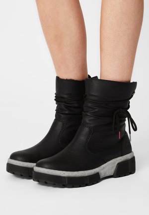 Black leather ankle boots with a slouch design, textured finish, lace closures, and a chunky white sole with tread patterns.