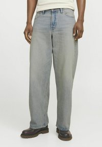 Jeans bleus clairs, amples, en denim, avec taille haute et jambes droites, portés avec des bottes marron foncé.