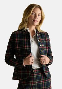 Tartan blazer with navy, green, and red pattern, gold buttons, structured collar, paired with a white blouse featuring a ruffled neckline.