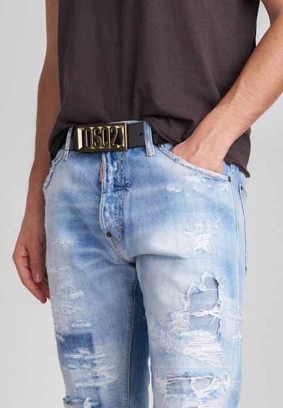 Jeans in denim azzurro chiaro con strappi e orli sfrangiati, abbinati a una cintura nera con una fibbia logo dorata.