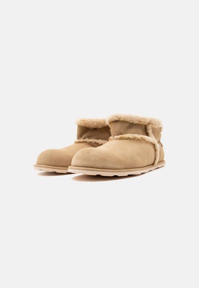 Paire de bottines beiges en daim avec doublure en shearling duveteuse et semelles en caoutchouc, conçues pour la chaleur et le confort.