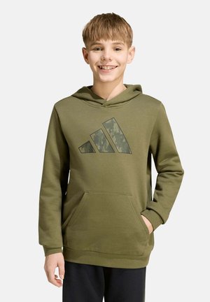 Un garçon souriant porte un sweat à capuche vert olive avec un logo camouflage et une poche avant, sur un fond uni et clair.