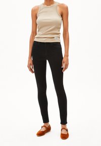 Beige linne, smala svarta jeans och rostfärgad platt skor med rem. Outfiten har en figurnära silhuett och mjuka texturer.