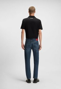 Crna pamučna polo majica u kombinaciji s plavim trapericama. Polo majica ima ovratnik i detalj s logotipom na leđima. Traperice su slim-fit kroja s crvenom oznakom na stražnjoj strani.