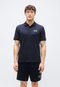 Mornarsko modra polo majica z ovratnim vratnim izrezom, kratkimi rokavi in logotipom EA7. Kombinirana z ujemajočimi mornarsko modrimi hlačami, oba izdelana iz gladke tkanine.