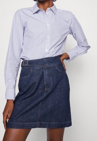 Ljusblå och vitrandig skjorta med knappar och krage, i kombination med en mörkblå denimkjol med bälte i midjan och synliga sömmar.