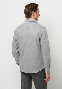 Grijze flanellen shirt met een kraag, knoopmanchetten en een gebogen zoom. De stof is gestructureerd en heeft een subtiel gemêleerd patroon.