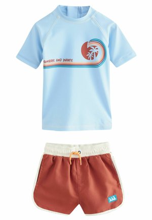 Rash guard bleu clair à manches courtes avec le texte et le graphique "RAYONS DE SOLEIL ET VAGUES", associé à un short de bain orange-brun avec une bordure blanche.