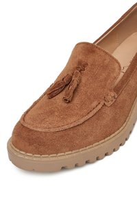 Pruun nahast loafers, ümarate varvastega, dekoratiivsete tupsudega ja paksu beeži välispinna taldiga, millel on õmblemise detailid ülemise ääre ümber.