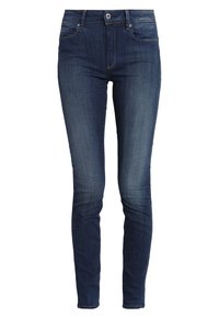 Jeans ajustados en denim azul oscuro. Presentan un efecto deslavado cerca de los bolsillos y las costuras. Diseño clásico de cinco bolsillos con cremallera y cierre de botón.