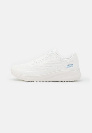 Sapatilha desportiva branca com um upper de malha respirável, design texturizado, frente com atacadores e uma sola de borracha flexível com um leve salto.
