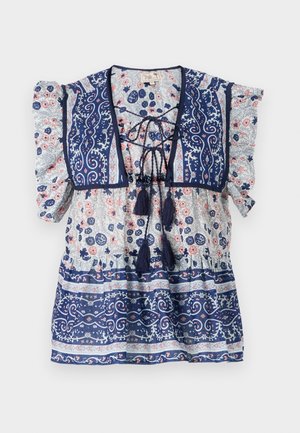 Blusa floral azul marinho com mangas bufantes, frente com cordão, franja e padrões intrincados em azul claro e pêssego, feita de tecido leve.