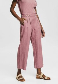 Lichtroze linnen broek met een hoge taille, wijde pijpen, plooien aan de voorkant en twee zijzakken, versierd met twee knopen op de taille.