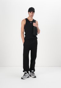 Sort ærmeløs tanktop med et lille frontlogo, sorte sweatpants, en sort kasket og sorte-hvide sneakers med markante striber.
