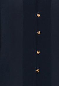 Blusa blu navy con una texture liscia, dotata di chiusura frontale con bottoni e bottoni dorati con un motivo intrecciato.