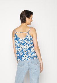 Camisola floral em azul com padrões de flores brancas e pretas. Apresenta alças finas e um design de costas curvas. Tecido leve.