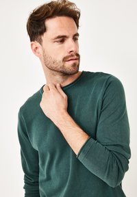 Dunkelgrünes Langarmshirt mit Rundhalsausschnitt aus strukturiertem Stoff, mit gerippten Bündchen und einem lockeren Schnitt.