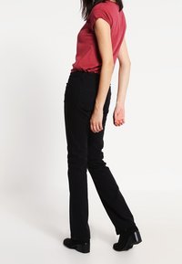 Pantalons noirs à jambe droite associés à un haut à manches courtes et col rond rouge, mettant en valeur une texture lisse et un design ajusté.