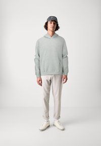 Lichtgrijze hoodie met een V-hals, zachte textuur en lange mouwen. Gecombineerd met crèmekleurige aansluitende broeken en witte sneakers.