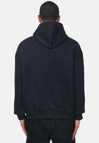 Crna oversized dukserica s kapuljačom na vezanje, rebrastim manžetama i donjim dijelom, od mekanog materijala, bez vidljivih logotipa ili uzoraka, prikazana sa strašne strane.