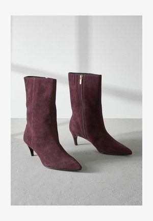 Botas de tobillo de ante burdeos con punta afilada y un tacón pequeño, que cuentan con una cremallera lateral y una textura suave.